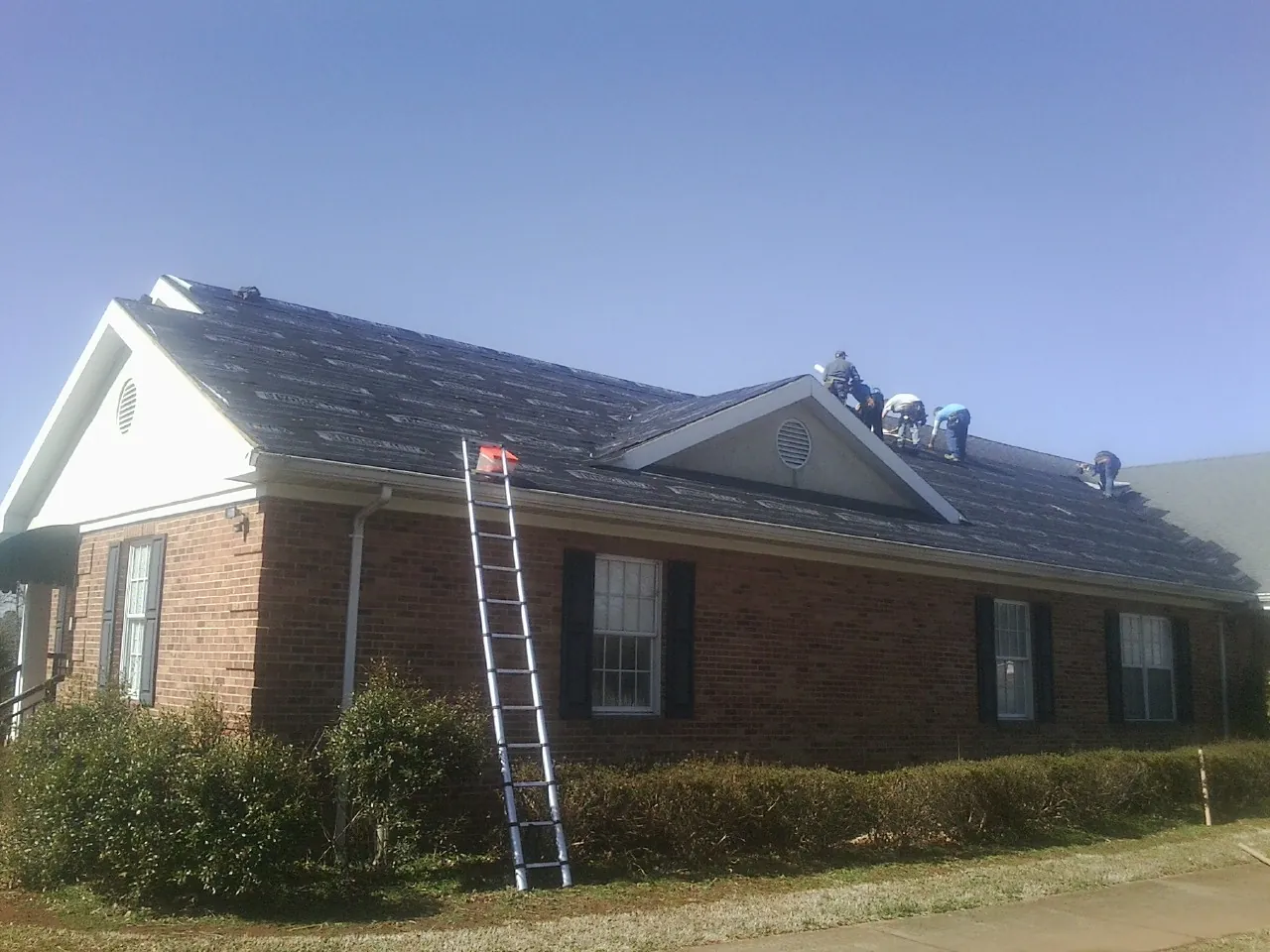 Crew tearing shingles off a brick ranch roof with a ladder set — Emergency Roof Repair work by our crew in Riegelsville