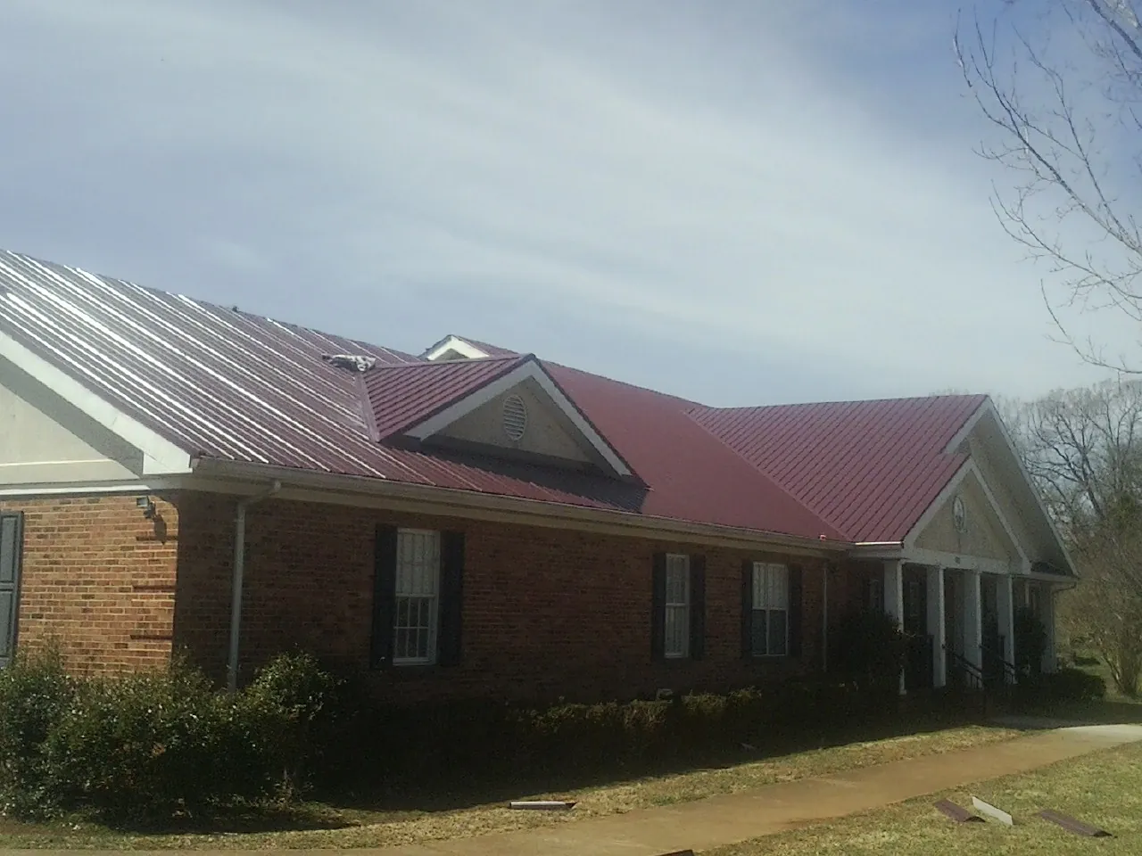 Red metal roof with gabled entries on a long brick building, from a Hail Damage Roof Repair job in Riegelsville