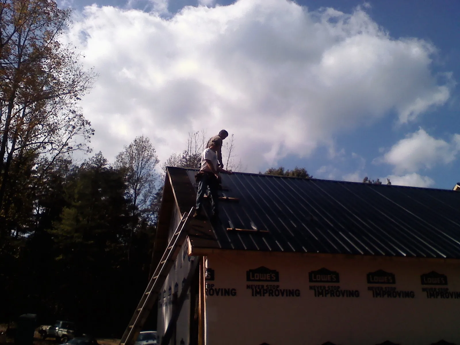 Roofer fastening dark metal panels high against a cloudy sky, from a Roof Inspection job in Riegelsville