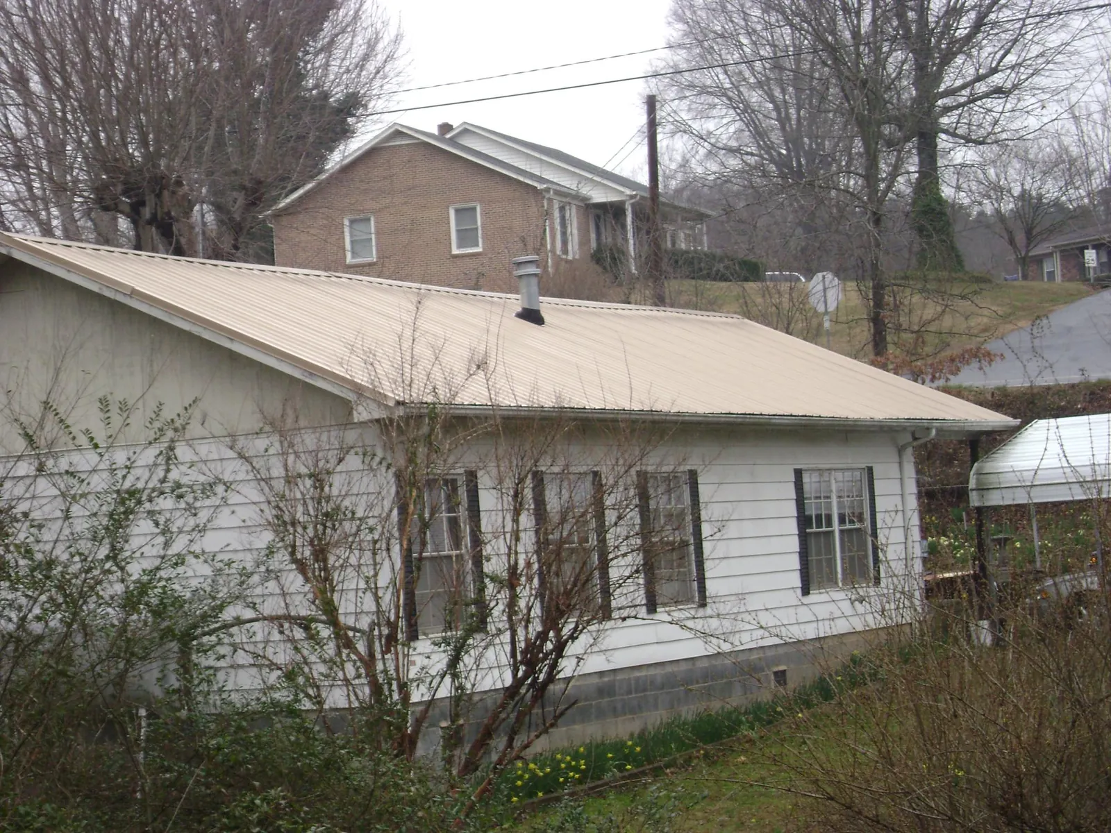 Tan metal roof on a white sided house set into a hillside — Commercial Roofing by Roofing Brothers in Riegelsville
