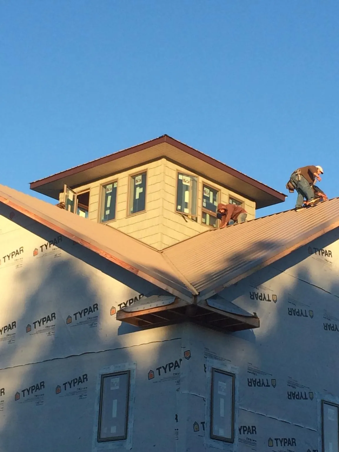 Roofers working around a rooftop cupola on a new metal roof at sunset in Riegelsville